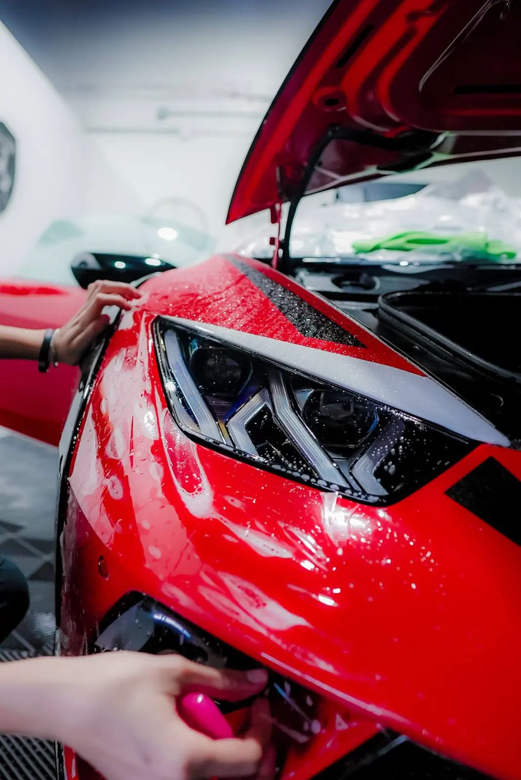 Installer squeegeeing paint protection film onto a red supercar